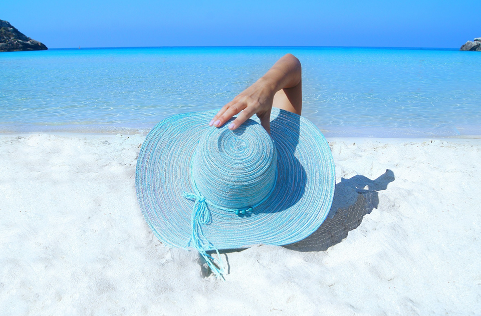 protecting your skin, Sunscreen: Enjoying The Summer Sun In A Healthy Way, image of a woman on the beach with a hat
