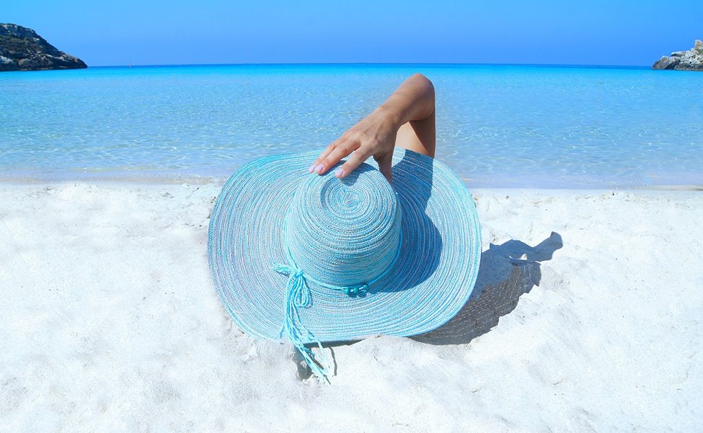 protecting your skin, Sunscreen: Enjoying The Summer Sun In A Healthy Way, image of a woman on the beach with a hat